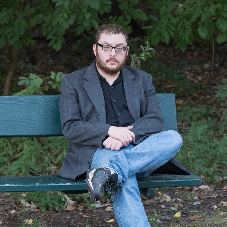 Image of TZ Krasner self published author of fantasy books centered around high power & action fights. He is sitting on a bench in a park.